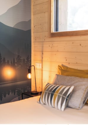 Ein Schlafzimmer mit Bett, Kissen, einem Nachttisch, einer Lampe und Wandbild.