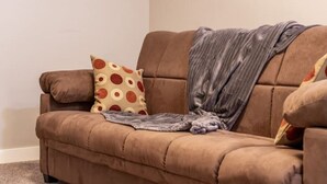A brown sofa with a polka dot pillow and a gray blanket. - Cove On A Hill - Entire (2Bdrm & Full Bath) Basement Suite (Calgary)