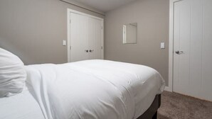 A bedroom with a bed, two white doors, and a small mirror on the wall. - Cove On A Hill - Entire (2Bdrm & Full Bath) Basement Suite (Calgary)