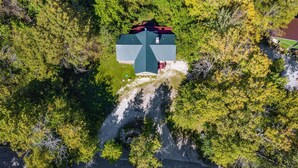 Une vue aérienne d’une maison entourée d’une forêt dense, avec une allée bien visible menant à l’entrée.