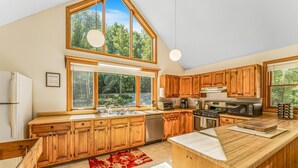 Une cuisine spacieuse avec des meubles en bois, un grand îlot central et une vue sur la forêt par les fenêtres.