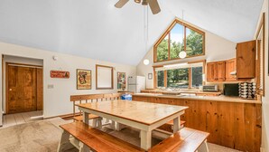 Une cuisine avec des meubles en bois, une grande fenêtre et un coin repas comprenant une table et des bancs en bois.