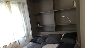 A bedroom with a bed, a built-in shelving unit, and a window with curtains.