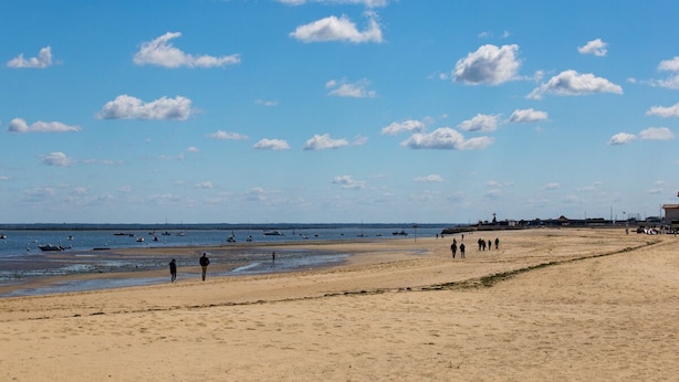 A wide sandy beach with a clear sky and scattered clouds.