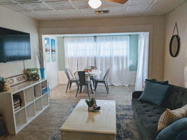 A living room with a flat-screen TV, a sofa, a coffee table, and a dining area with chairs and a table. - Tropical Tiny House (New Port Richey)