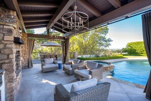 A covered outdoor seating area with wicker furniture and a pool. - Casa Azul - Mediterranean Resort-Style Home (Thousand Oaks)