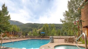 A pool area with a hot tub, lounge chairs, and a view of mountains. - Silver Mill 8153 by Summit County Mountain Retreats (Keystone)