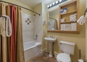 A bathroom with a bathtub, a sink, and a toilet. There are towels and a mirror on the wall.