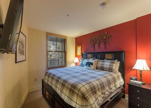 A bedroom with a bed, a nightstand, a lamp, a window with blinds, and a wall-mounted decoration.