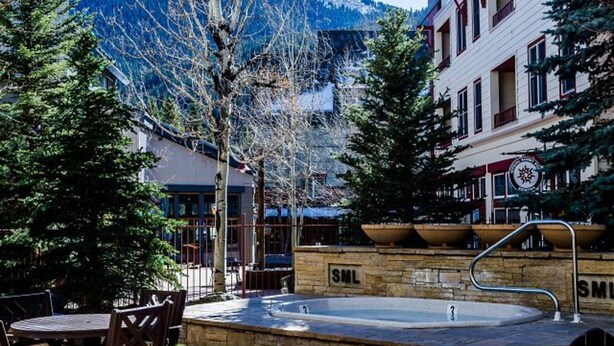 A courtyard with a stone fountain, outdoor seating, and buildings with a mountain backdrop. - Silver Mill 8153 by Summit County Mountain Retreats (Keystone)