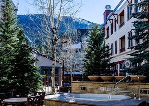 A courtyard with a stone fountain, outdoor seating, and buildings with a mountain backdrop. - Silver Mill 8153 by Summit County Mountain Retreats (Keystone)