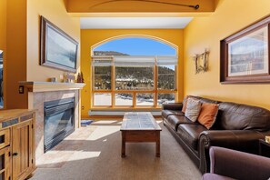 A living room with a fireplace, a leather sofa, a coffee table, and a large window with a view of a snowy landscape.