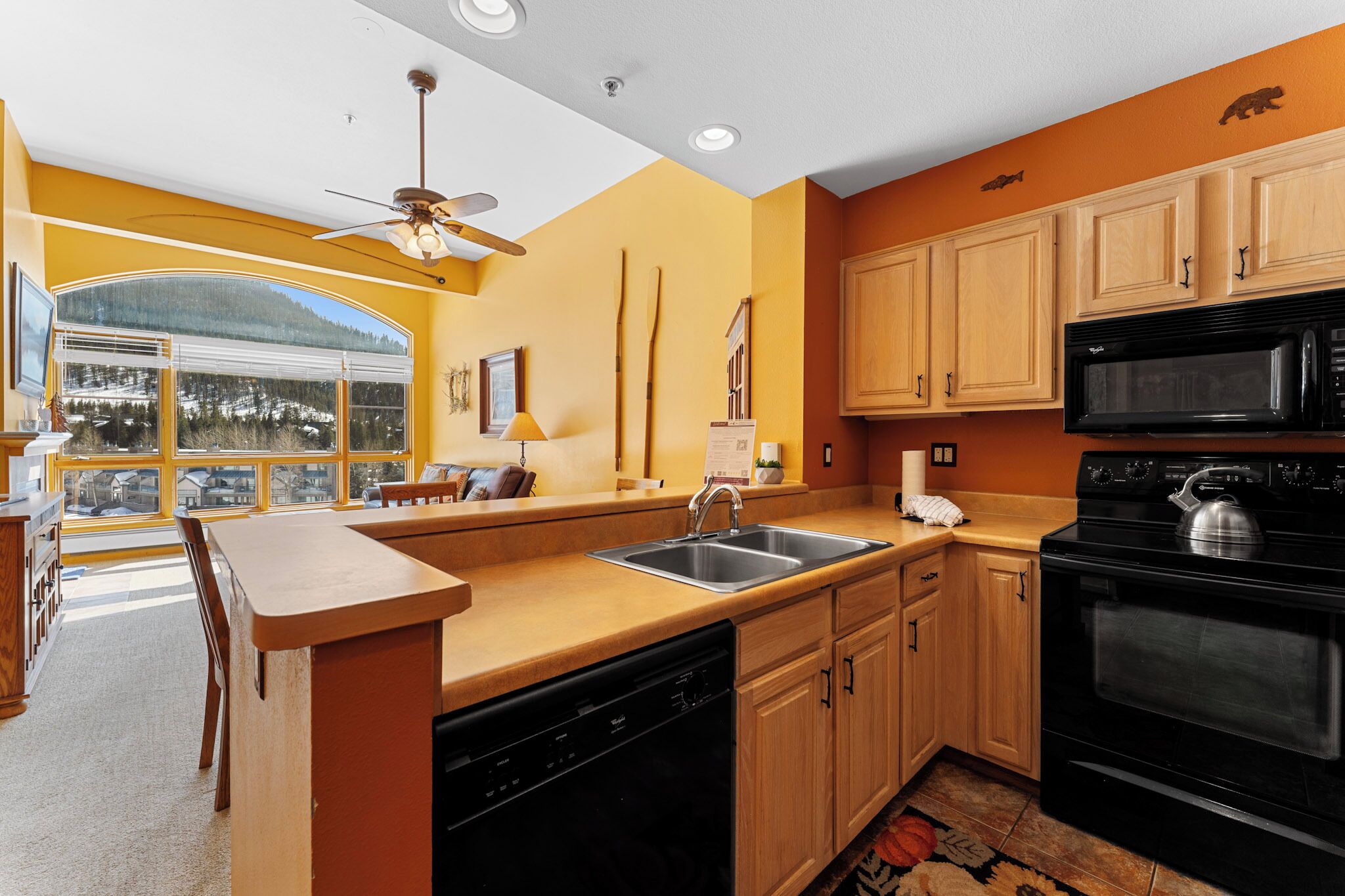 A kitchen with wooden cabinets, a black stove, and a large window with a view of a snowy landscape.