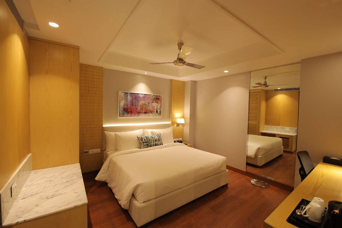 A hotel room with a large bed, a desk with a coffee maker, a mirror, and a ceiling fan.