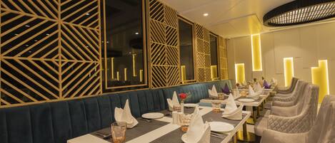A restaurant with a long dining table, cushioned seating, and decorative wall panels.