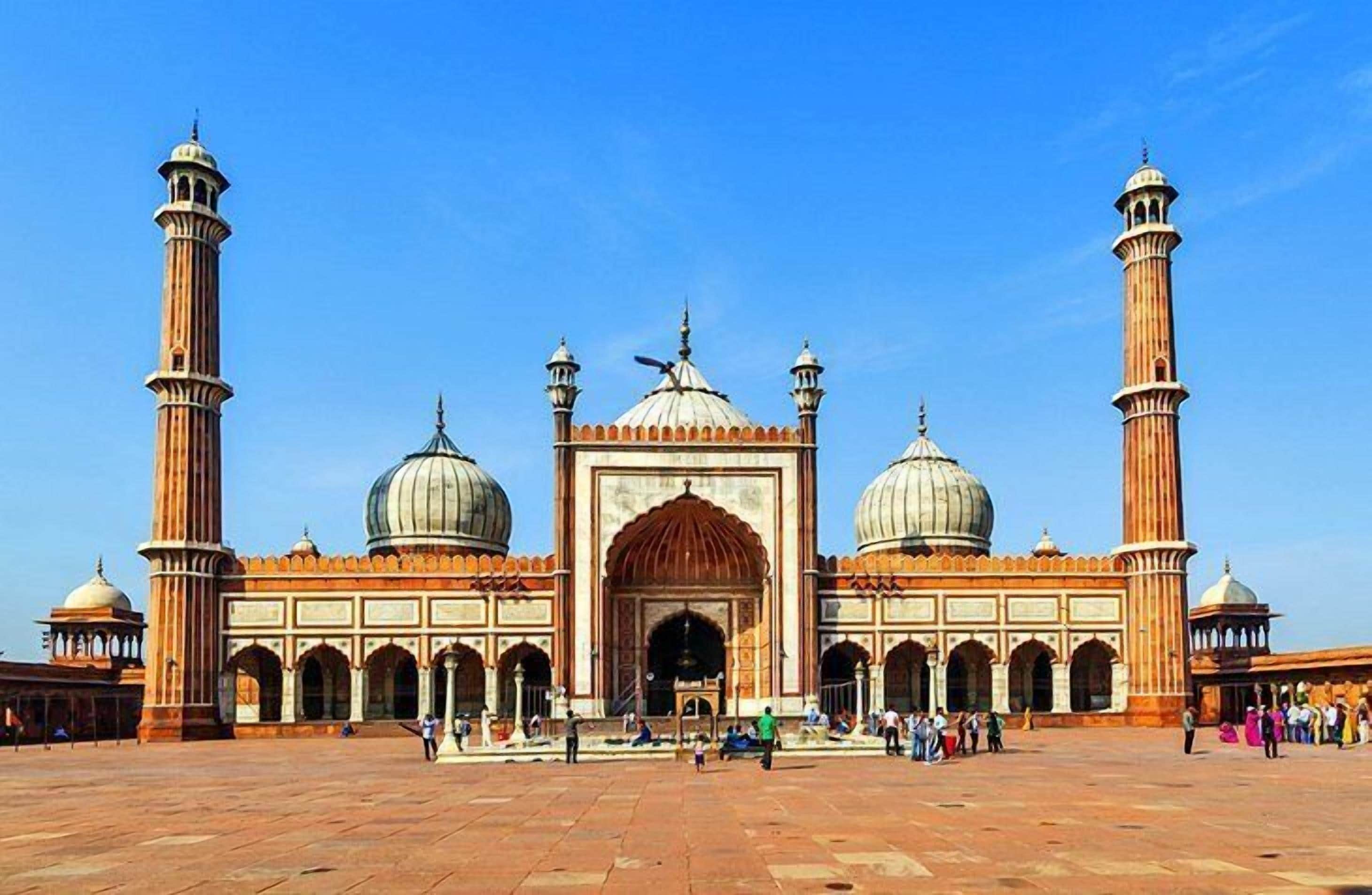 A large, historic building with multiple domes and minarets, featuring a central archway and a spacious courtyard.