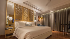 A hotel room with a large bed, a wooden nightstand with a lamp, a mirror, and a blue chair. - Best Western Darbar (New Delhi)