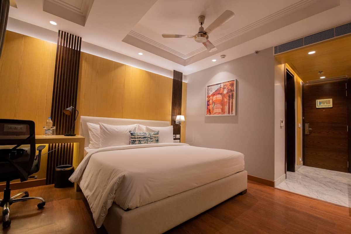 A hotel room with a bed, desk, chair, and a door.