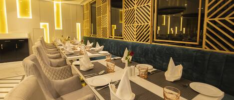 A restaurant with a long dining table set for a meal, cushioned chairs, and decorative wall panels.