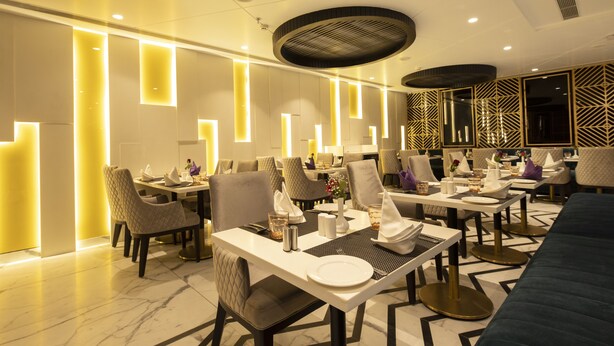 A modern dining area with multiple tables and chairs, equipped with place settings and ambient lighting. - Best Western Darbar (New Delhi)