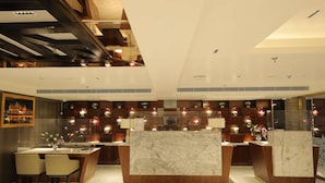 A modern hotel lobby with marble reception desks, a dining area with chairs, and decorative lighting. - Best Western Darbar (New Delhi)