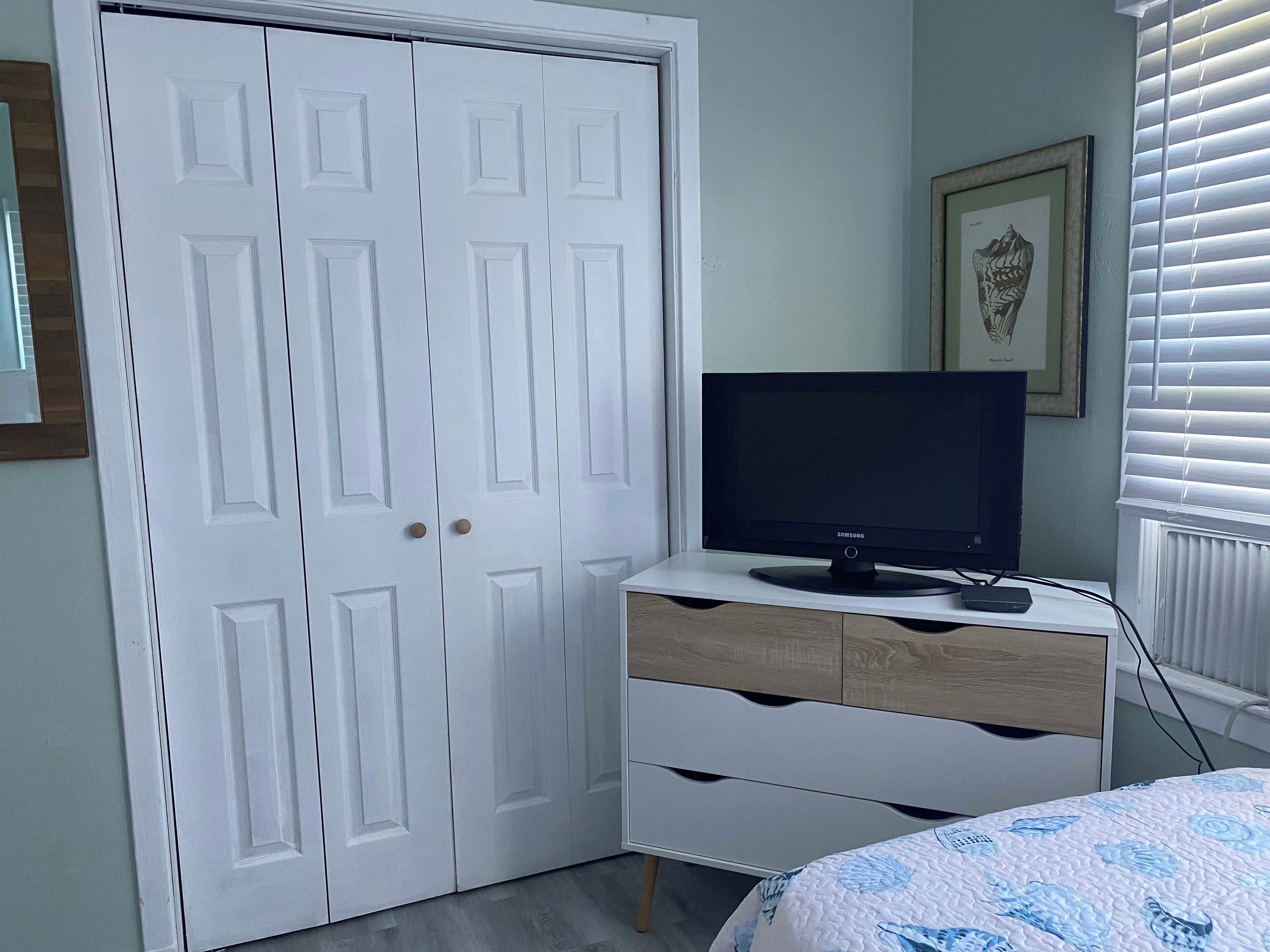 A bedroom with a white wardrobe, a television on a wooden dresser, and a bed with a blue floral bedspread.
