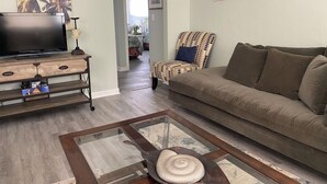 Una sala de estar con una televisión, un sillón estampado, un sofá y una mesa de centro.