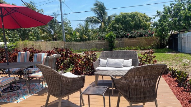 Un patio con mobiliario de mimbre, un paraguas rojo y una mesa.