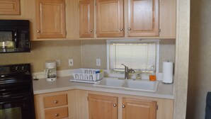 A compact kitchen with wooden cabinets, a microwave, a coffee maker, and a sink.