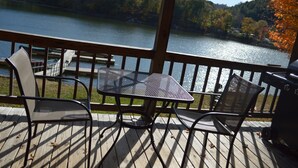 A wooden deck with a table and chairs overlooking a lake, surrounded by trees.
