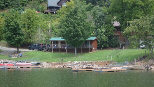 A cabin with a deck overlooking a lake, surrounded by trees.