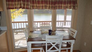 A dining area with a table set for four, white chairs, and a plaid valance over the windows.