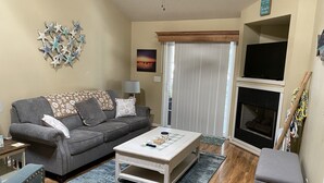 A living room with a grey sofa, a coffee table, a TV, a fireplace, and a wall with starfish decorations. - Pet Friendly Townhome Between Ocean Isle and Sunset Beach (Ocean Isle Beach)