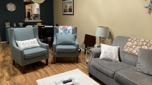A living room with two armchairs, a sofa, a coffee table, a lamp, and a dining area in the background. - Pet Friendly Townhome Between Ocean Isle and Sunset Beach (Ocean Isle Beach)
