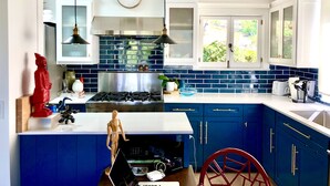 A modern kitchen with blue cabinets, a stainless steel stove, and a window with a view of greenery. - Peaceful Hillside Garden Cottage (Los Angeles)