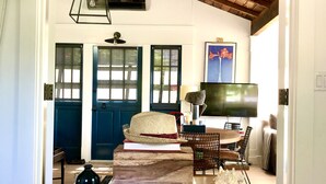 A room with a high ceiling, wooden beams, a TV, a dining table with chairs, a bookshelf, and a patterned rug. - Peaceful Hillside Garden Cottage (Los Angeles)