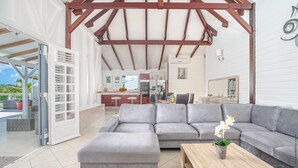 A spacious living area with a grey sectional sofa, a wooden coffee table, and a sliding glass door leading to an outdoor patio. - Villa Cacyli: private heated pool and Jacuzzi, view of Baie des Mulets (Le Vauclin)