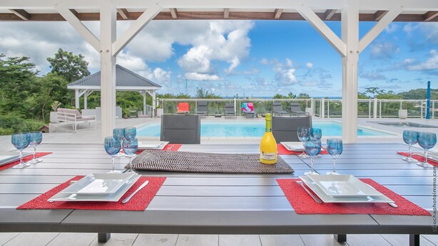 An outdoor dining area with a pool view, red placemats, and a bottle of champagne. - Villa Cacyli: private heated pool and Jacuzzi, view of Baie des Mulets (Le Vauclin)