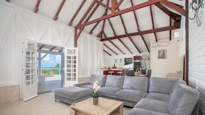 A spacious living room with a grey sectional sofa, a wooden coffee table, and a view of the outdoors. - Villa Cacyli: private heated pool and Jacuzzi, view of Baie des Mulets (Le Vauclin)