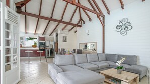 Un salón amplio con un sofá seccional gris, una mesa de centro de madera y una zona de comedor con una cocina al fondo.
