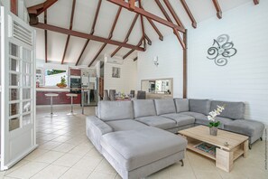 A spacious living area with a grey sectional sofa, a wooden coffee table, and a dining area with a kitchen in the background.