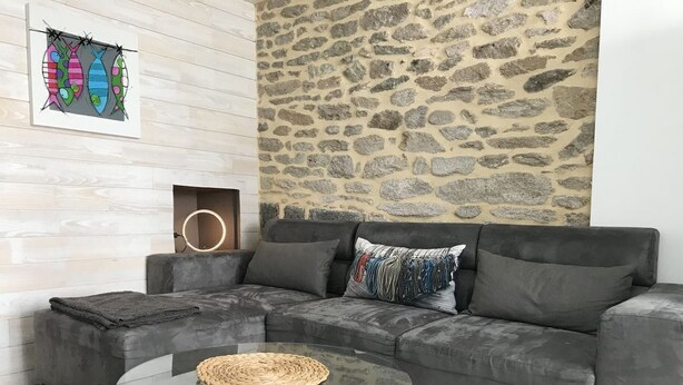 A modern living room with a grey sectional sofa, a glass coffee table, and a stone wall. - Charming fisherman's cottage with terrace 6 minutes walk from the beach (Quiberon)