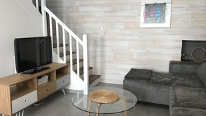 A modern living room with a wooden TV stand, a glass coffee table, a grey sofa, and a staircase with white railings. - Charming fisherman's cottage with terrace 6 minutes walk from the beach (Quiberon)