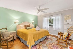 Ein Schlafzimmer mit Bett, Sessel, Nachttisch, Kommode und Deckenventilator.