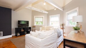 Un salon moderne avec un canapé blanc, un téléviseur posé sur un meuble noir et une table en bois sur laquelle se trouve une lampe.