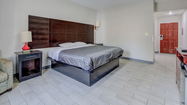 A modern hotel room with a large bed, a nightstand, a red door, and a hallway. - Plantation Inn & Suites Near Locust Grove I 75 (Jackson)