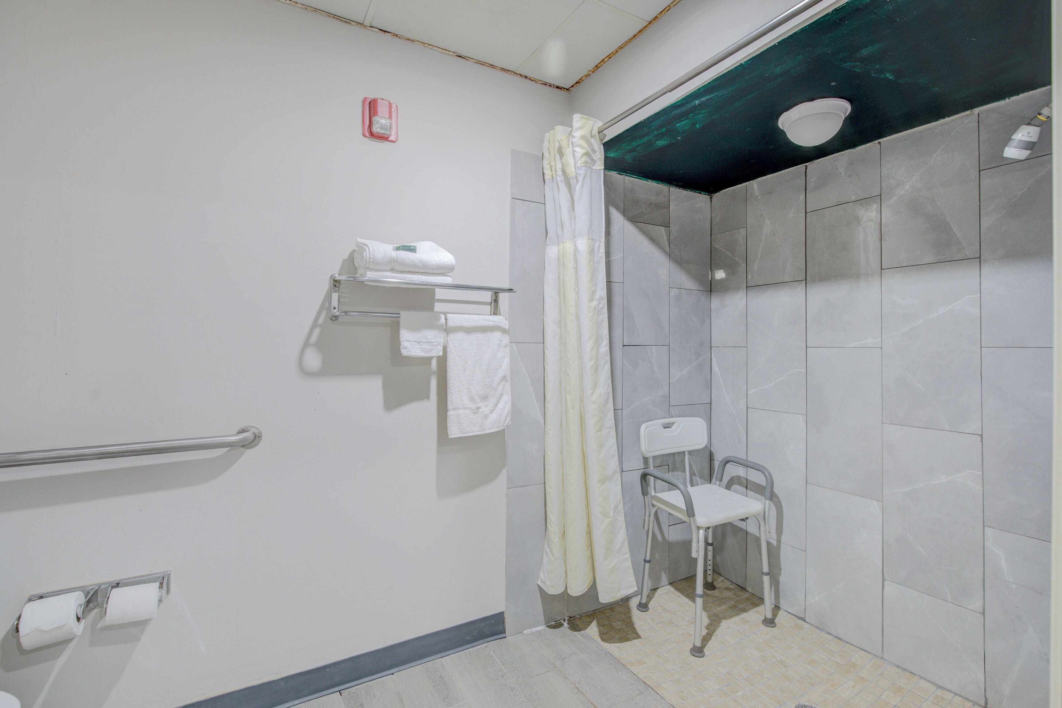 Un bagno con doccia, maniglione, sedia accessibile per sedie a rotelle e porta asciugamani.