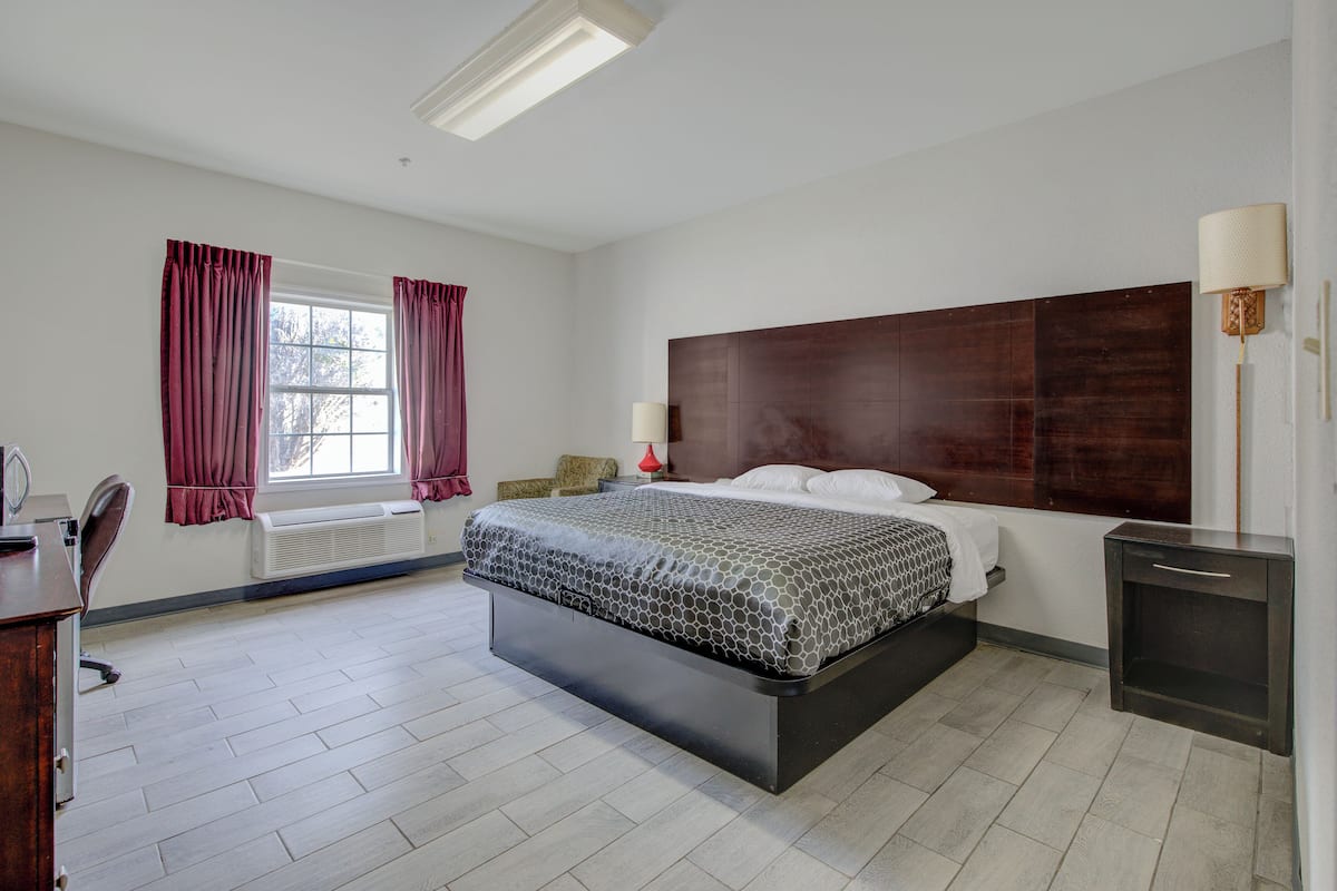 A modern bedroom with a large bed, a bedside table, a lamp, and a window with curtains.