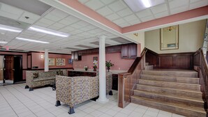 A lobby with a reception desk, patterned sofas, a staircase, and a tiled floor. - Plantation Inn & Suites Near Locust Grove I 75 (Jackson)