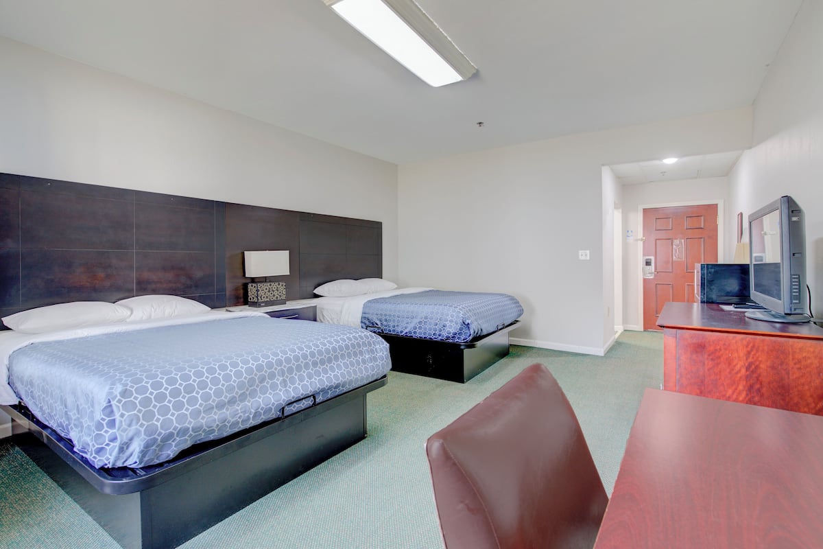 A hotel room with two beds, a desk, a chair, a television, and a door.